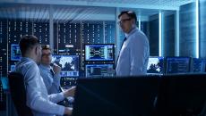 Three cybersecurity professionals talk in a network control room.