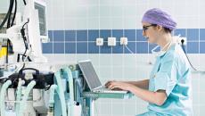 Healthcare worker using laptop near medical equipment