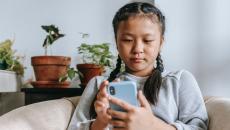 Young person sits on a couch and types on a mobile phone